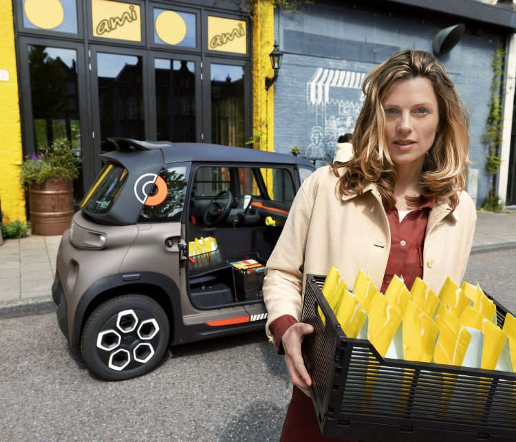 Жінка тримає коробку з багетами хліба біля Citroën Ami на вулиці