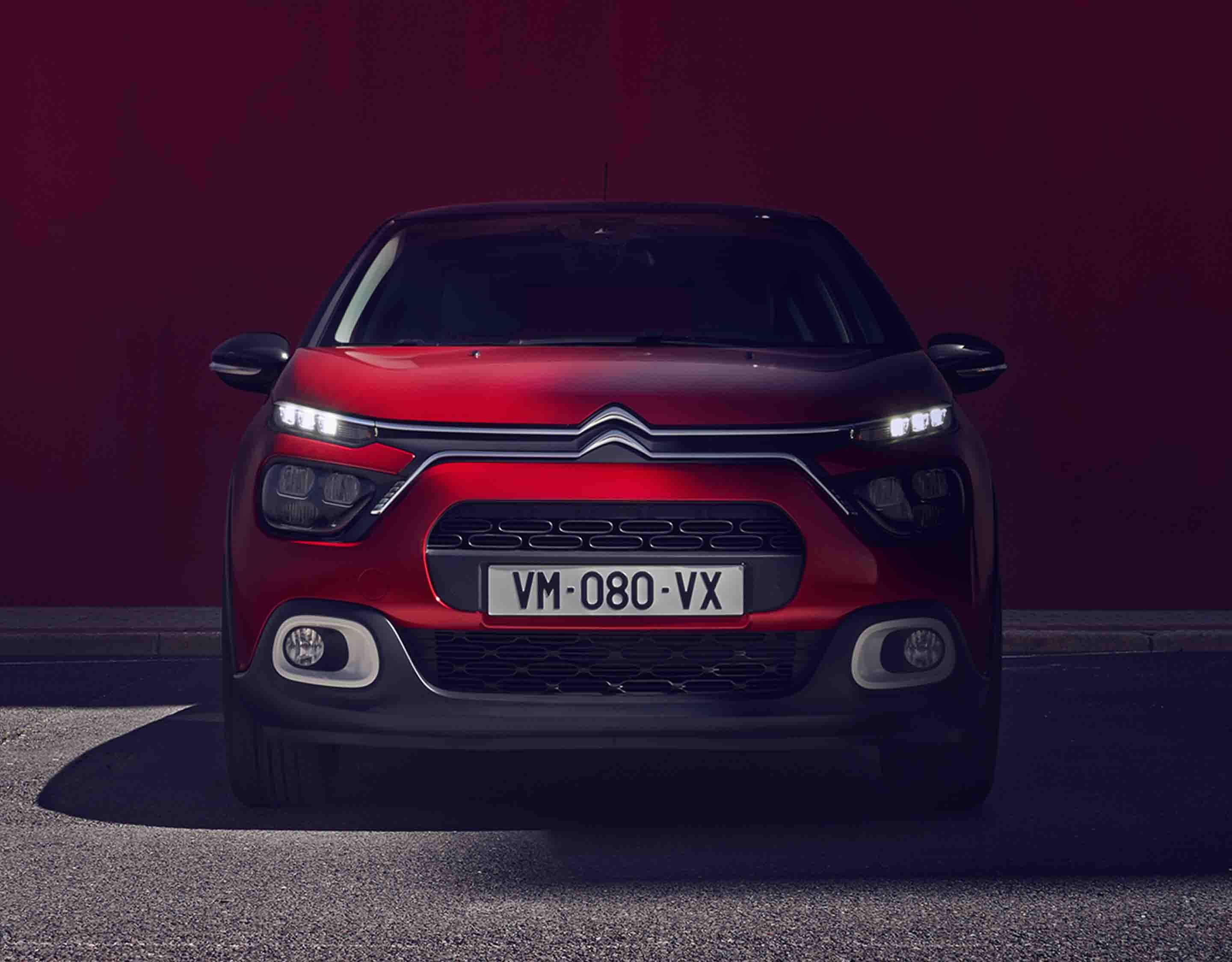 Citroen C3 червоного кольору, вигляд спереду з увімкненими приладами освітлення